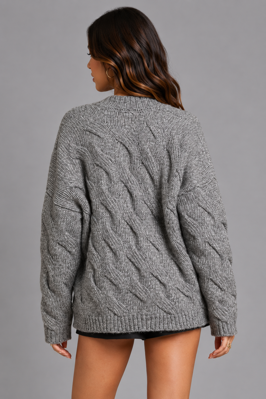 A woman shown from the back wearing a gray cable-knit sweater, photographed against a solid gray studio background.