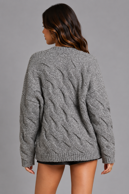 A woman shown from the back wearing a gray cable-knit sweater, photographed against a solid gray studio background.