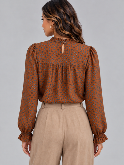 A woman shown from the back wearing a rust-brown long-sleeve blouse with a small geometric pattern and beige trousers, against a solid gray studio background.