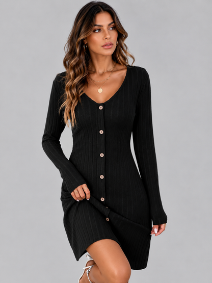 A woman modeling a black ribbed long-sleeve mini dress with a V-neck and front button closure, photographed against a plain light gray studio background.