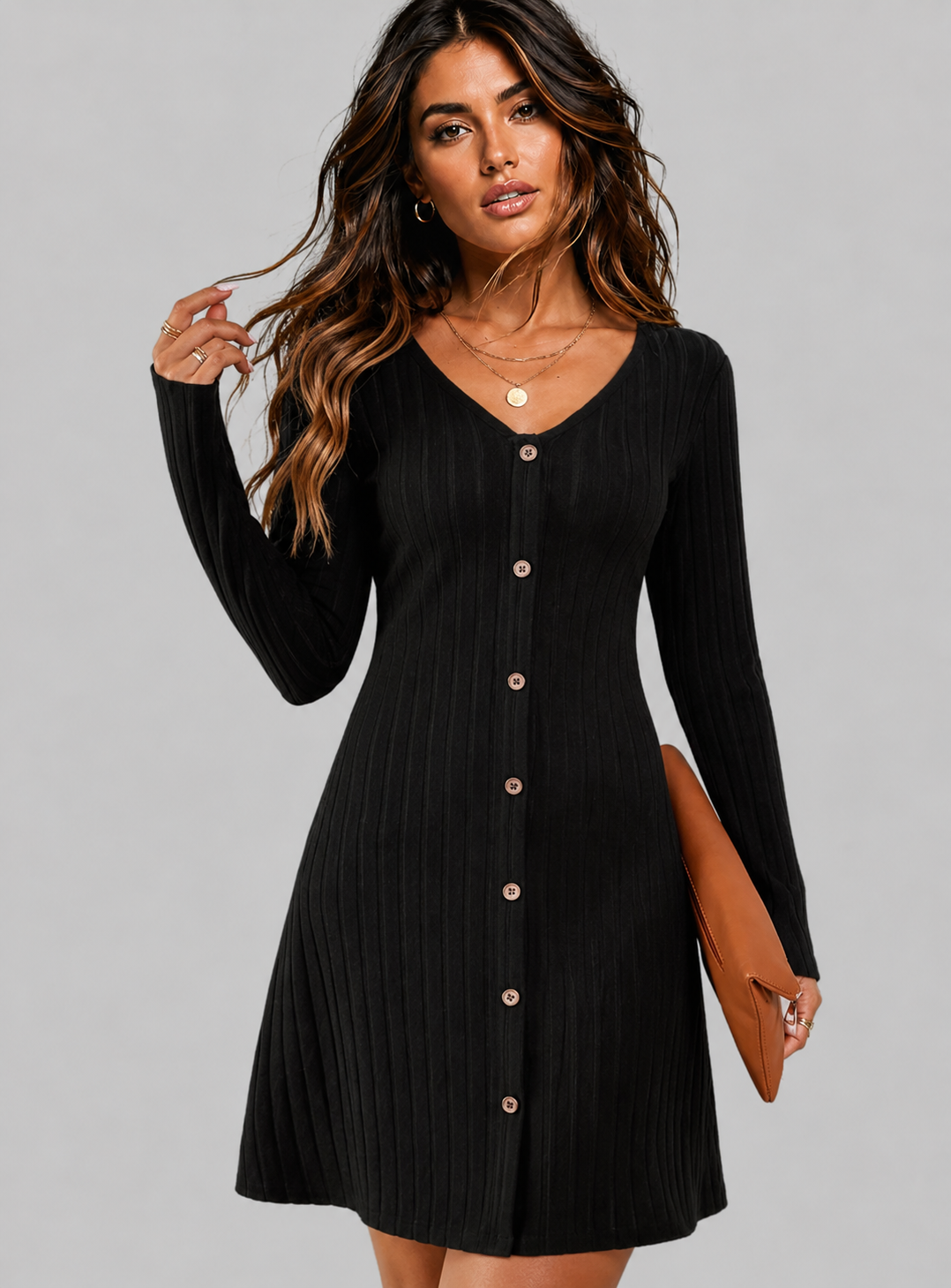 A woman modeling a black long-sleeve ribbed mini dress with a V-neck and button-front closure, holding a brown clutch against a plain light gray studio background.