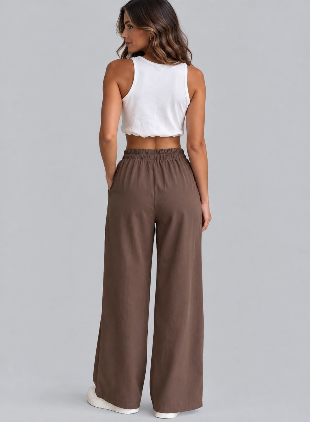 A woman shown from the back wearing a white sleeveless crop top and brown wide-leg pants against a light gray studio background.