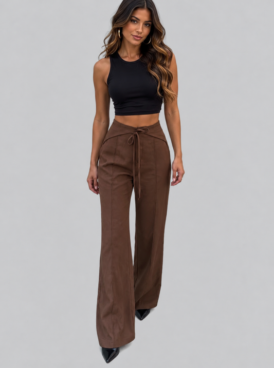 A woman modeling a black sleeveless crop top and high-waisted brown wide-leg pants with a drawstring waist, photographed against a solid light gray studio background.