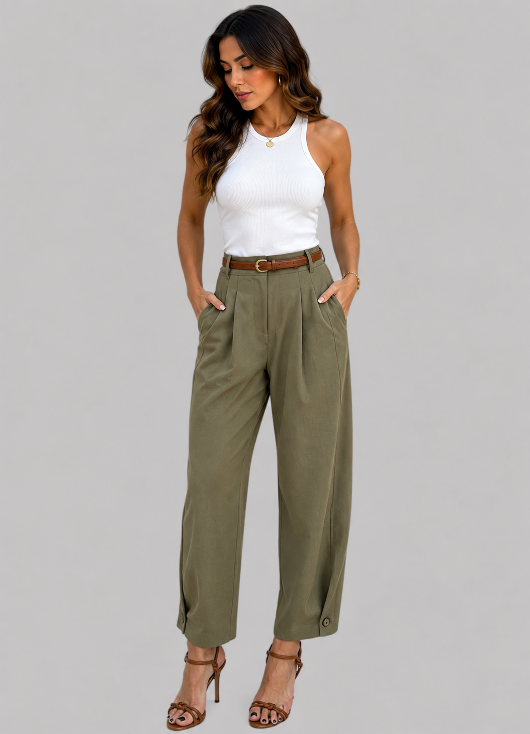 A woman modeling a pair of olive green wide-leg cropped pants with a brown belt, styled with a white sleeveless top and brown strappy heels against a solid gray background.