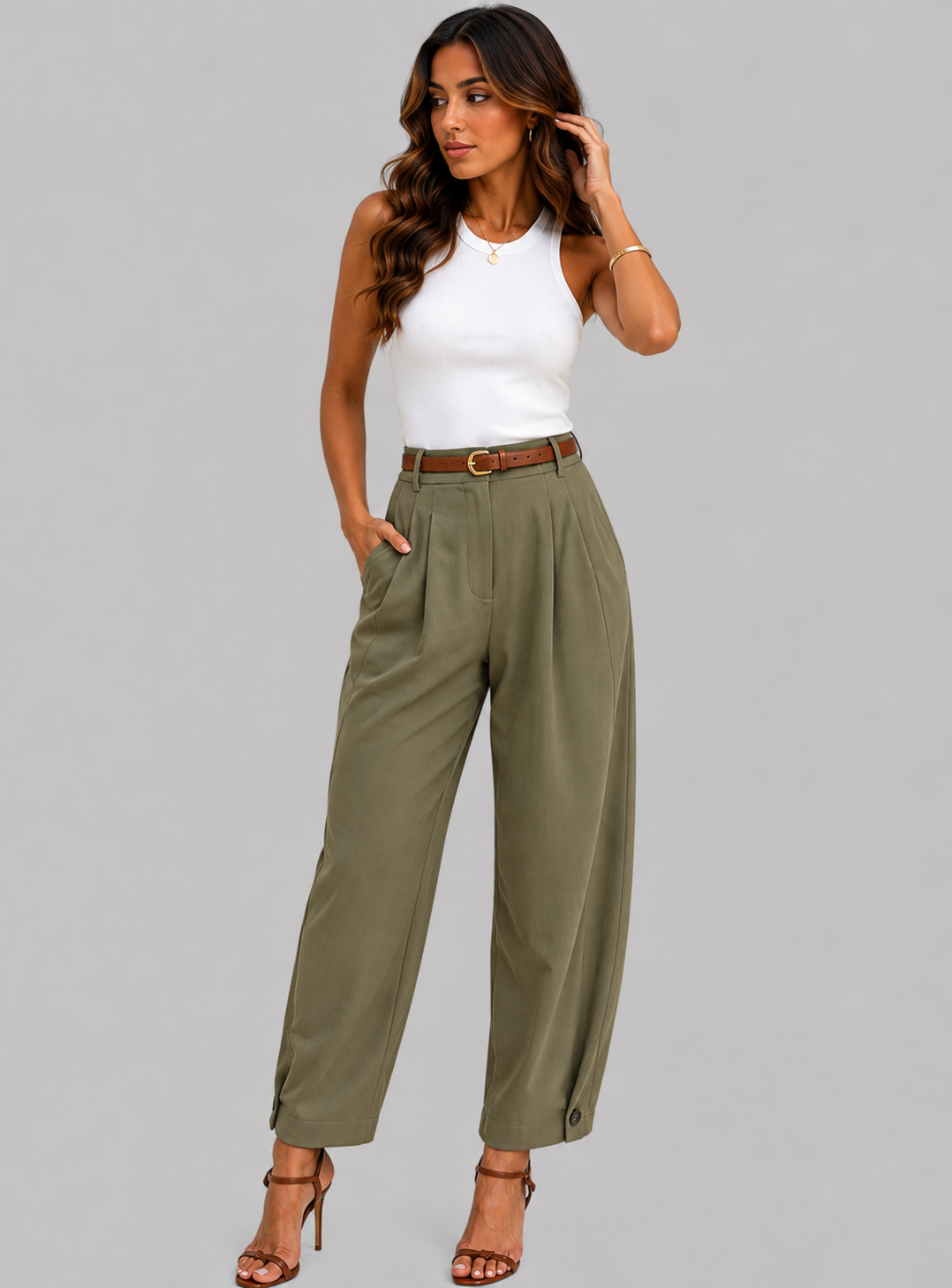 A woman modeling high-waisted, wide-leg olive green pants with a brown belt, paired with a white sleeveless top and brown strappy heels, against a solid gray studio background.