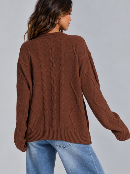 A woman shown from the back wearing a brown cable-knit sweater and light blue jeans against a plain gray studio background.