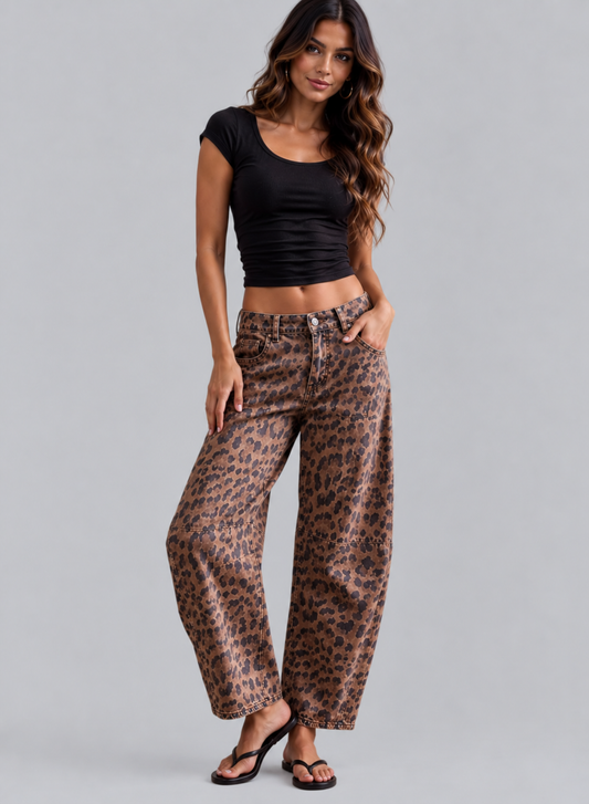 A woman modeling wide-leg leopard-print pants with a black crop top and black sandals, standing against a solid gray studio background.