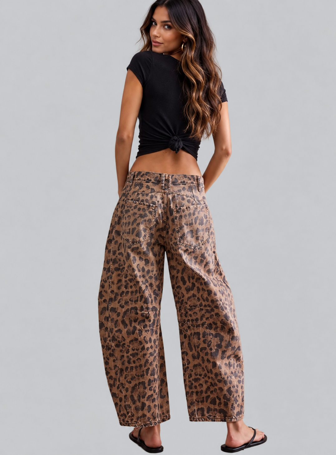 A woman shown from the back wearing leopard-print wide-leg pants and a black tied crop top, standing against a light gray studio background.