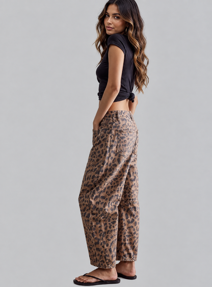 A woman modeling a pair of loose-fit leopard print pants, paired with a black cropped top and black sandals, photographed against a solid light gray studio background.