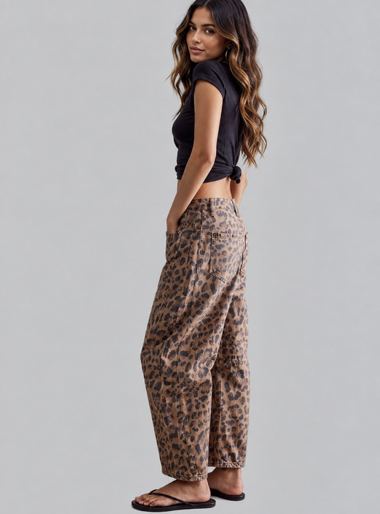 A woman modeling a pair of loose-fit leopard print pants, paired with a black cropped top and black sandals, photographed against a solid light gray studio background.