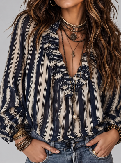 A close-up of a woman wearing a bohemian-style striped blouse with navy blue and beige vertical stripes, layered necklaces, and bracelets, paired with blue jeans.