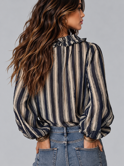 A woman shown from the back wearing a long-sleeve striped blouse with a ruffled high neck and voluminous balloon sleeves, paired with blue jeans against a solid gray studio background.