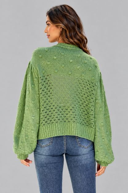 A woman shown from the back wearing a light green knit sweater with textured bobble details and balloon sleeves, paired with blue jeans, against a solid gray studio background.